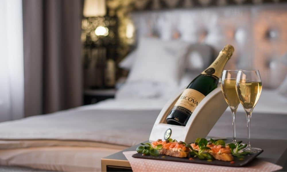 Bottle of sparkling wine with two glasses and canapés beside a hotel bed
