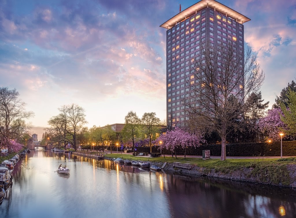 Hotel Okura Amsterdam tower beside a canal at dusk