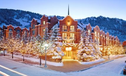 The St. Regis Aspen Resort in snow, with lit trees outside the entrance and Aspen Mountain behind
