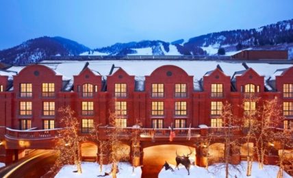 The St. Regis Aspen Resort's red-brick façade at dusk in winter, with ski runs on Aspen Mountain behind
