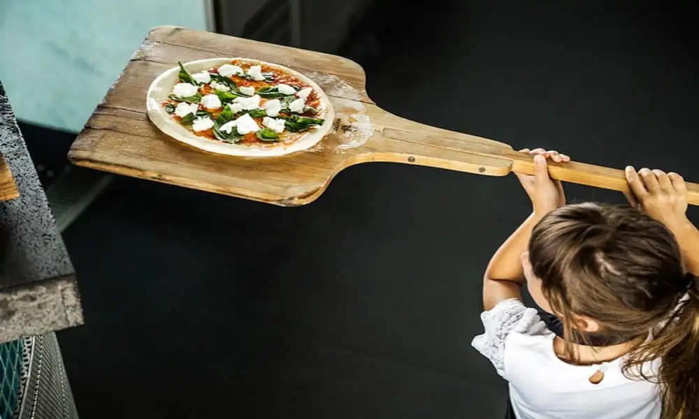 Child carrying a pizza on a wooden peel at COMO Point Yamu, Phuket