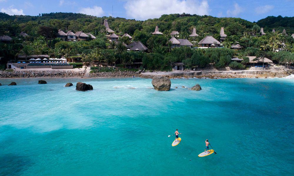 Paddleboarders in the bay below the thatched villas at NIHI Sumba