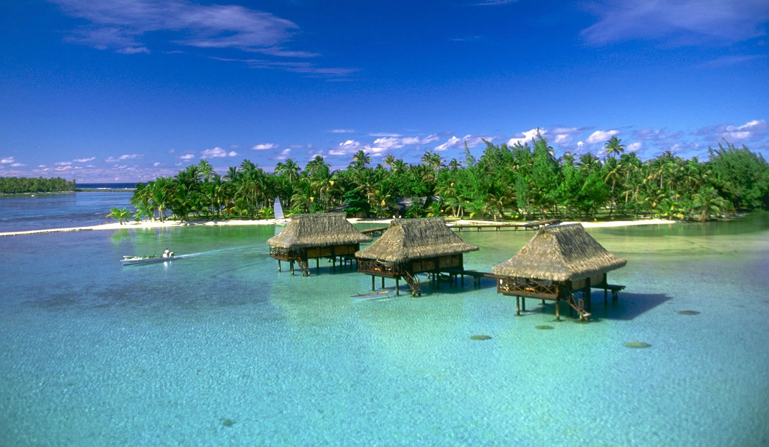 Three thatched overwater bungalows in the lagoon at Vahine Private Island, Taha'a