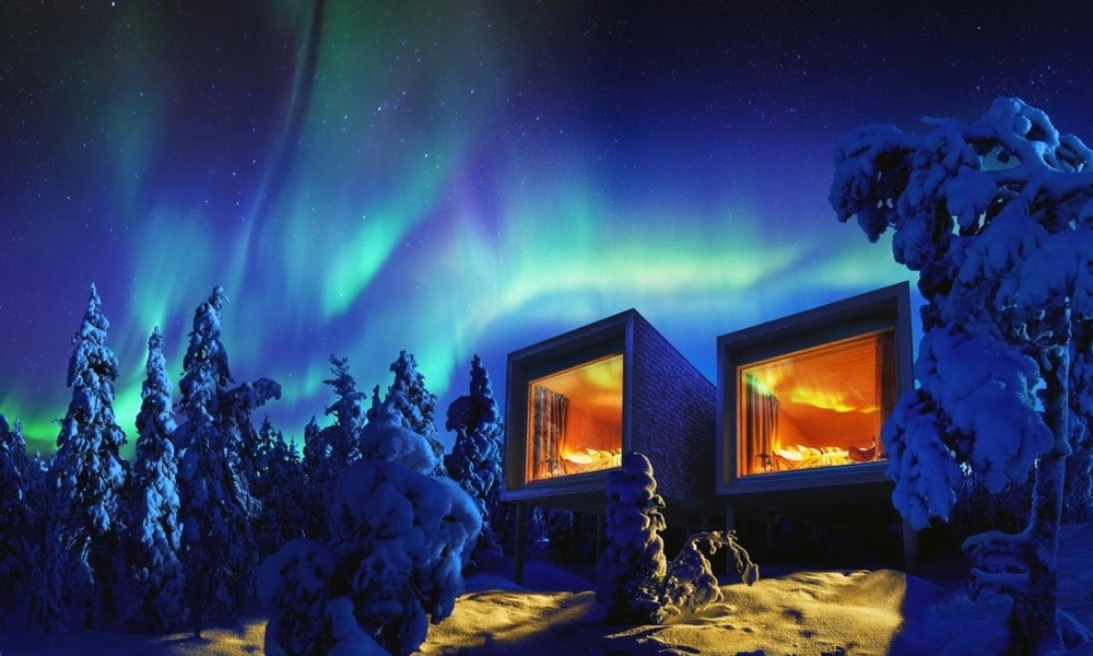 Two Arctic TreeHouse Hotel suites on stilts with lit panoramic windows under the northern lights