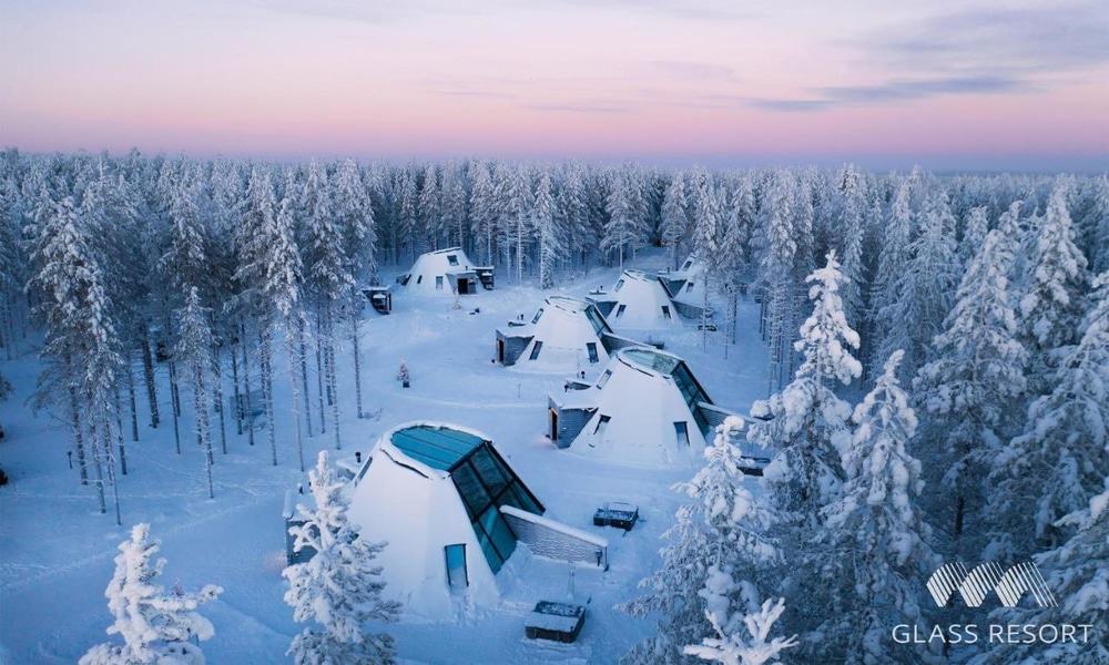 Glass Resort's kota-shaped glass apartments among snow-covered trees at dusk, Rovaniemi