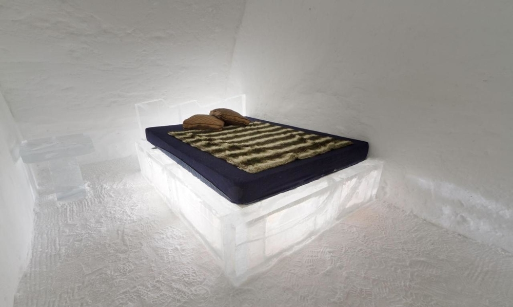 Regular suite at Hôtel de Glace with a bed on an ice base, a fur throw and snow walls (a past season)