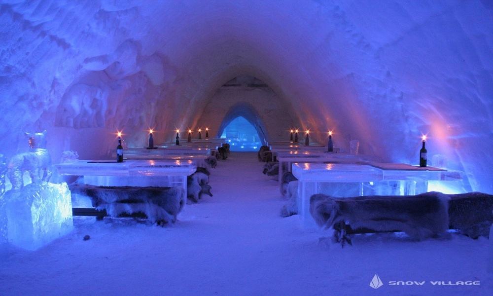 Ice restaurant at Lapland Hotels SnowVillage with ice tables, fur-covered benches and candles under a snow vault (a past season)