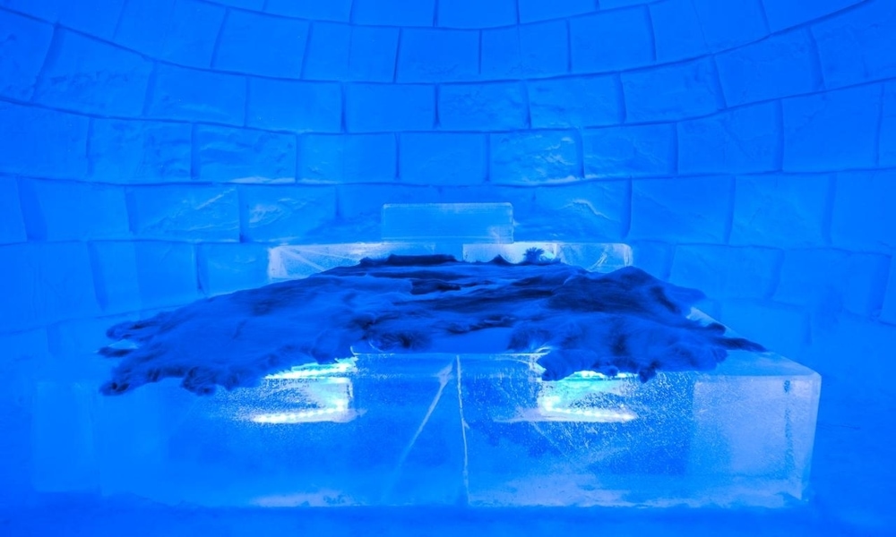 Igloo room at Sorrisniva with an ice bed under reindeer hides inside a wall of ice blocks lit blue