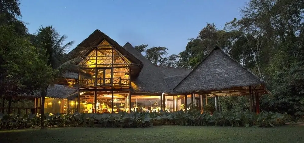 The main lodge at Inkaterra Reserva Amazónica, lit at dusk, with a thatched roof